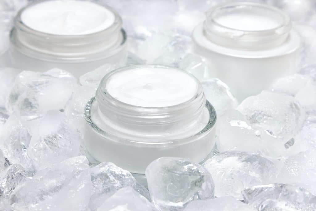 Close-up of glass jar with cream surrounded by ice cubes