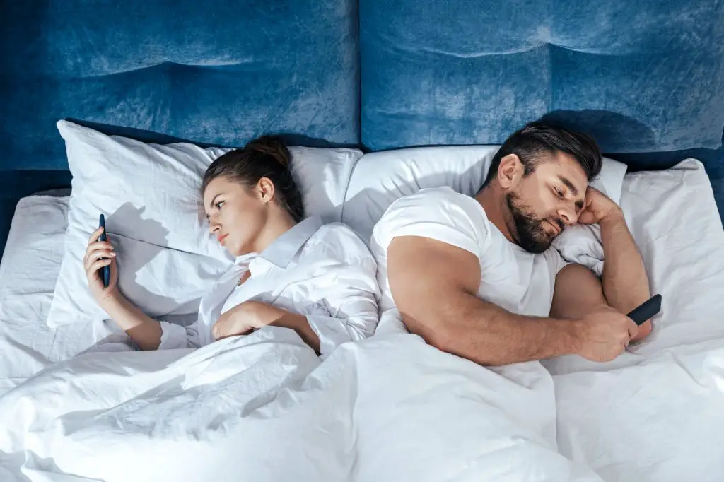 Portrait of young couple using smartphones in bed