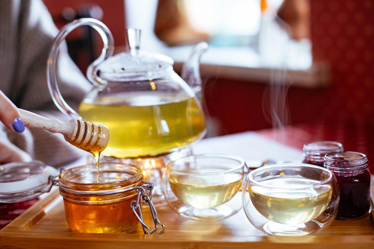 Warm tea served with honey in glass cups on wooden tray.
